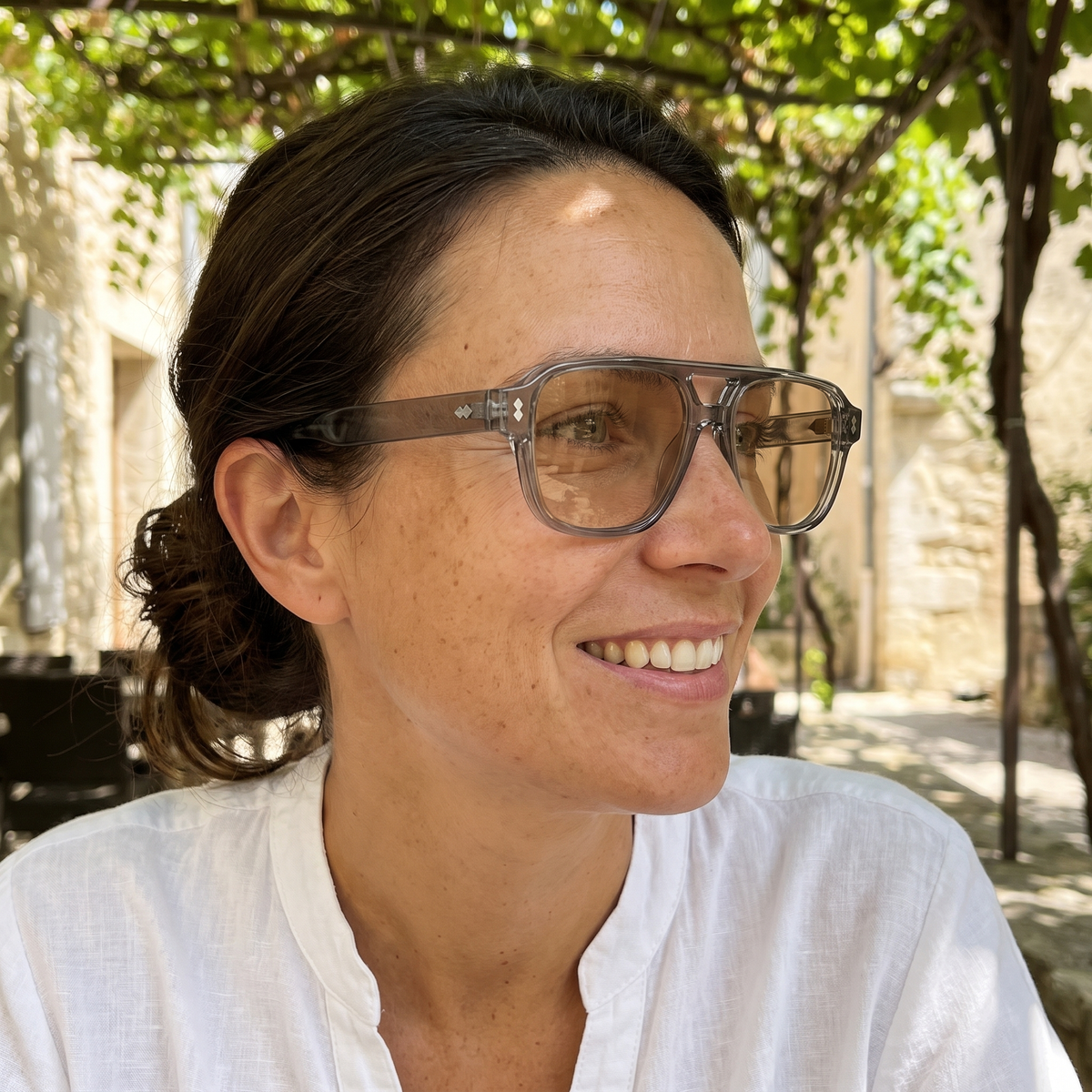 Femme portant Le Zéphyr Ambre à l'ombre, monture transparente, verres légèrement teintés