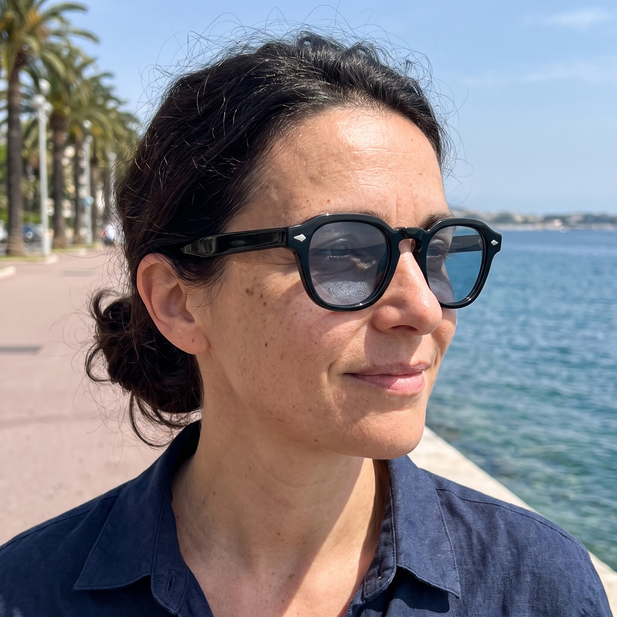 Femme portant Le Sirocco Capri Blue au soleil, monture noire brillante, verres bleus teintés